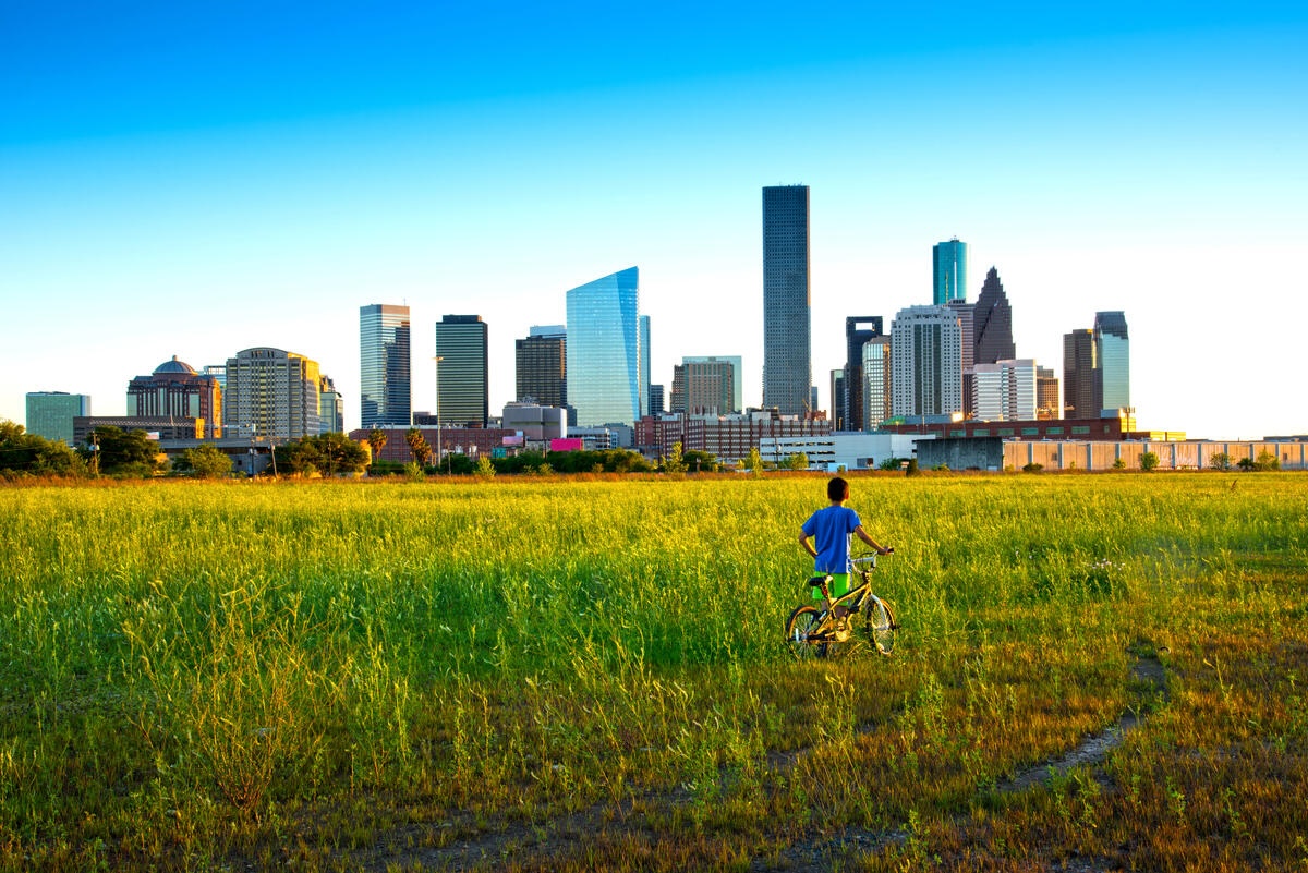 A young boy with his bicycle looks toward the imposing skyline of Houston