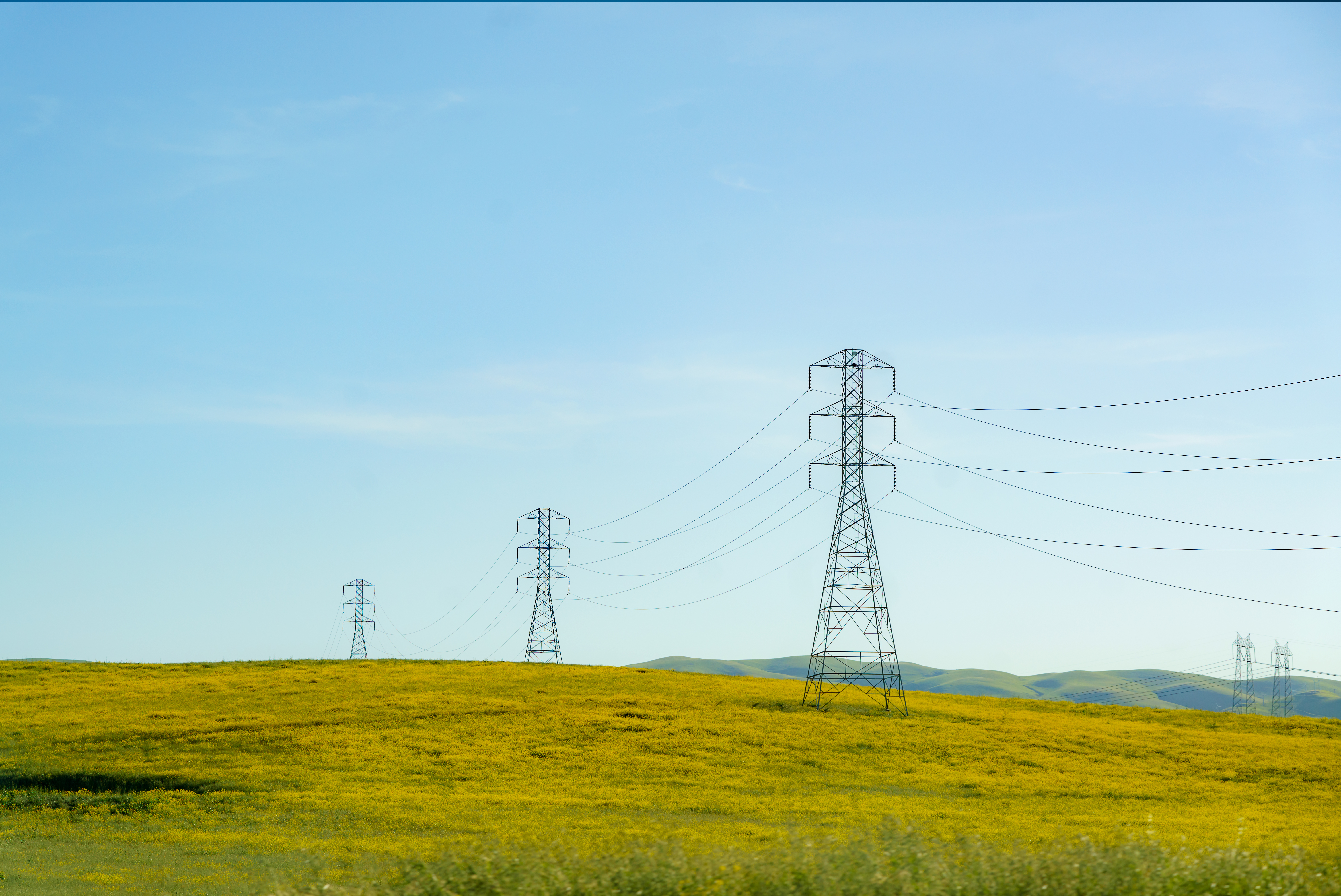 High-tension lines cut across rolling hills, weaving a modern energy network amidst the natural landscape.