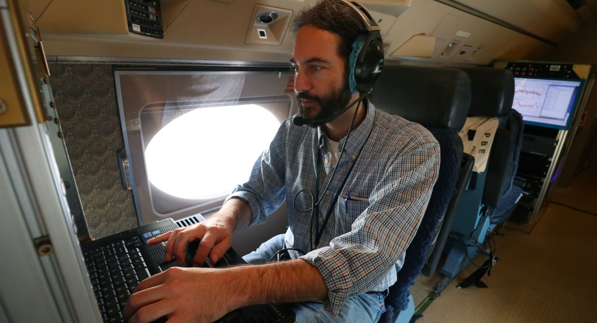 A man wearing headphones operates a technology console inside an aircraft