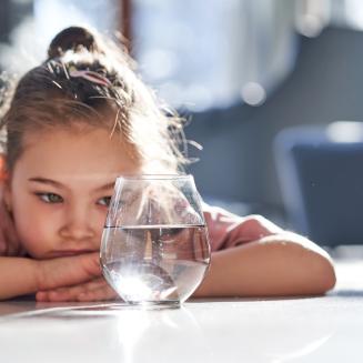 A small child looking at a glass of water.