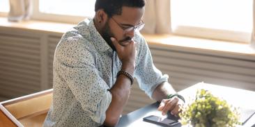 Man sitting at a desk looking thoughtfully at a cell phone